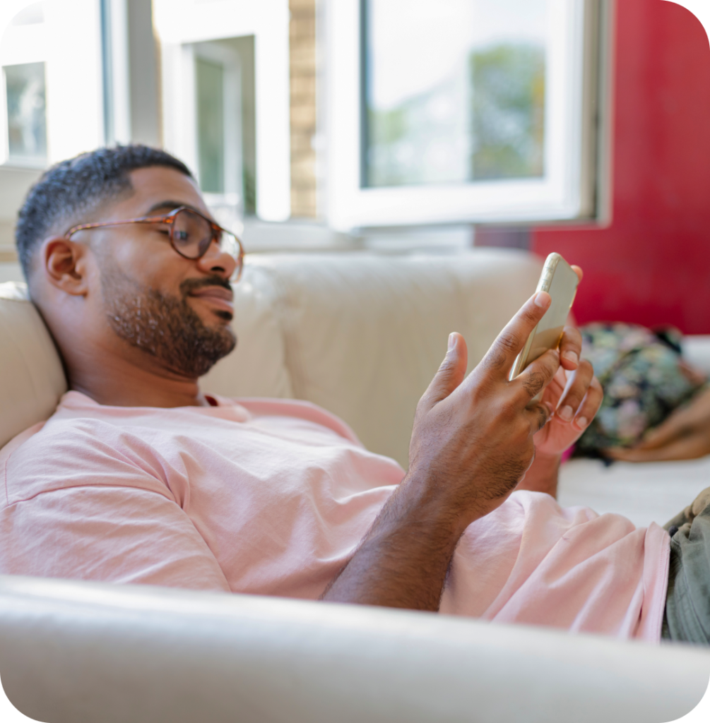 a man looking at a smartphone while reclining on a sofa